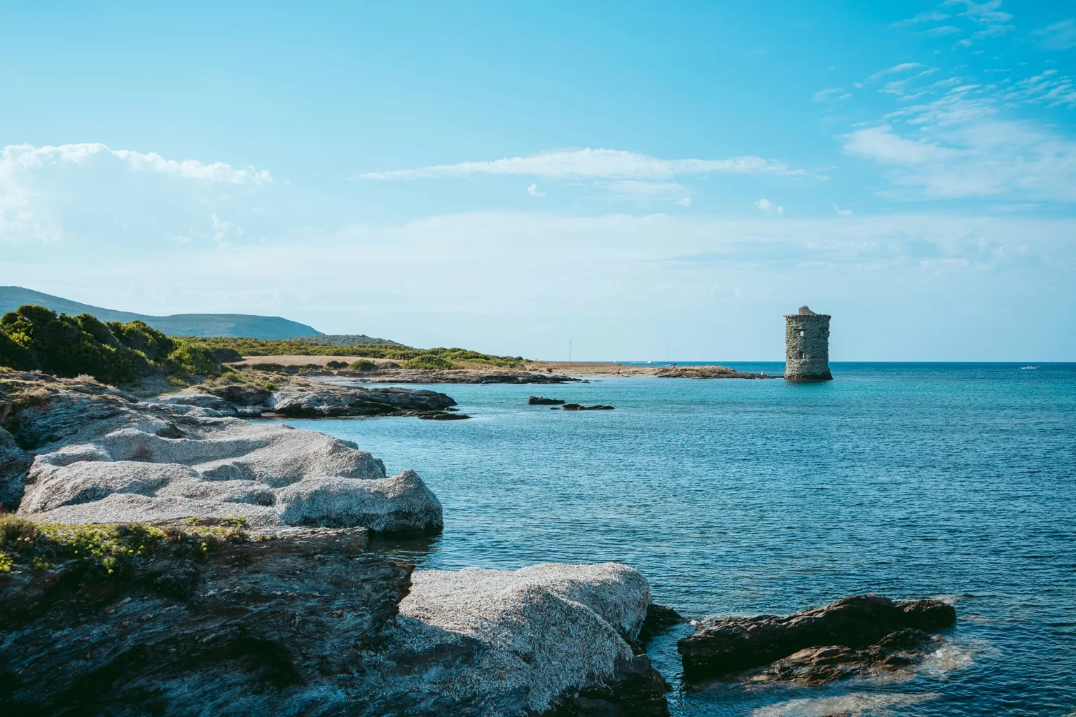Une tour de pierre au bord d’une mer turquoise, sur la côte corse